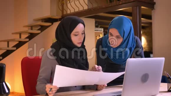 两位成功的穆斯林女企业家在头巾上的特写肖像用不同的图表比较数据视频的预览图