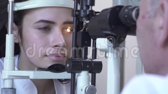 美丽的年轻女子在诊所做眼科检查坐在医生面前穿着白色的医疗外套看着验眼机视频的预览图