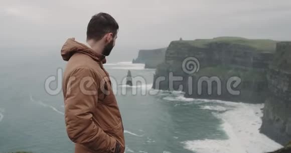 快乐的游客来到了令人惊叹的爱尔兰莫赫悬崖之地他站在悬崖的岸边感受着视频的预览图