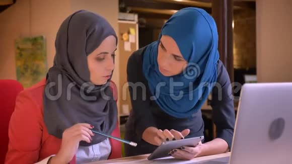 两位年轻的穆斯林女商人在笔记本电脑前讨论一个工作主题的特写肖像雇主指导视频的预览图