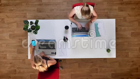 两个精力充沛的女孩坐在木制办公室的桌子旁用笔记本电脑和蓝屏视频的预览图