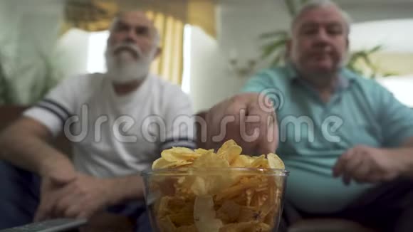 特写两个在家看电视的成熟的老人的画像朋友在吃薯条的时候看足球视频的预览图
