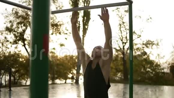 年轻人在户外的水平杆上做运动手臂上挂着的副横杠的健美操训练视频的预览图