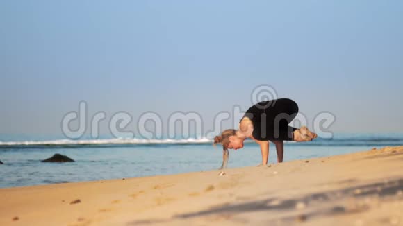 穿黑色运动服的金发女孩在海边练习瑜伽视频的预览图
