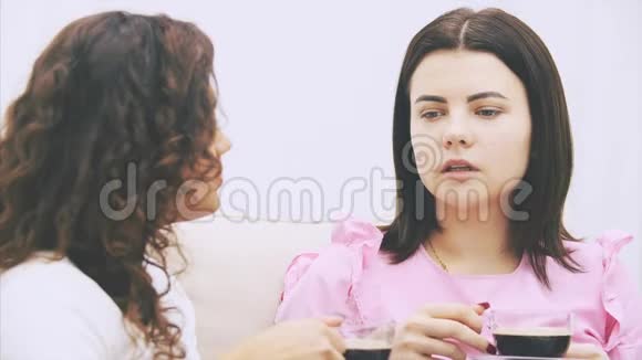两个女朋友在温暖的家环境中坐在沙发上喝着咖啡视频的预览图