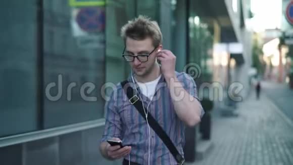 戴眼镜的年轻人在街上散步时享受音乐视频的预览图
