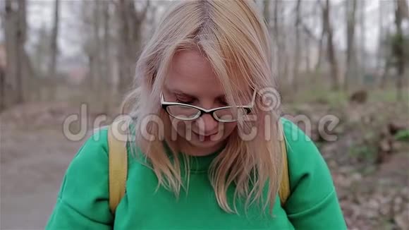 女孩坐在公园的长凳上向下看然后抬头看相机视频的预览图