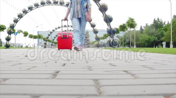 穿运动鞋的女人走路车轮上滚动一个红色的手提箱一个女人拿着她的手提箱走在街上概念视频的预览图
