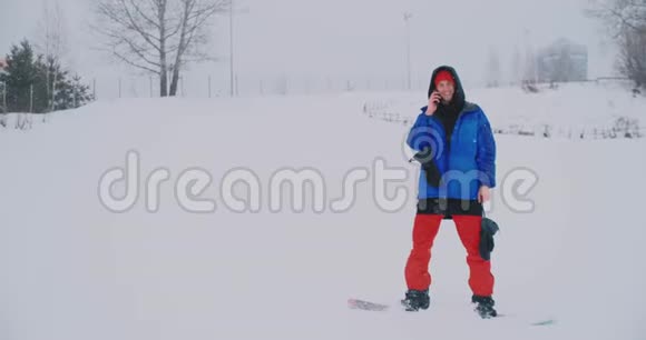 穿蓝色夹克的男性滑雪者在滑雪场的智能手机上直播视频的预览图