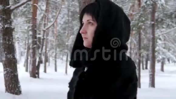 摄像机在这个女人周围近距离移动一个穿着黑色外套的黑发女孩站在森林或公园里在冬天下雪视频的预览图
