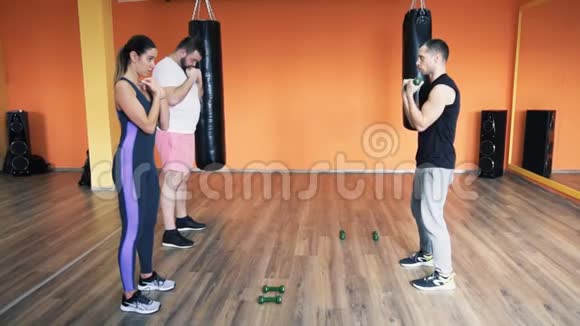 私人教练向一个胖男人解释苗条的女孩在健身房哑铃训练个人减肥训练视频的预览图