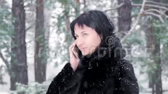 在一个冬天下雪的日子里相机滑块绕着一个女人站在公园或森林旁边一个黑发女孩视频的预览图