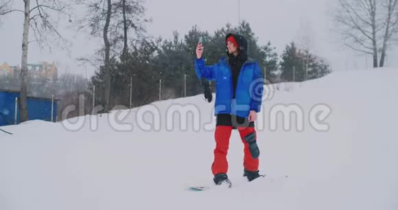 穿蓝色夹克的男性滑雪者在滑雪场的智能手机上直播视频的预览图