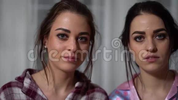 一对长着严肃面孔的漂亮妹妹双胞胎的肖像其中一个用手掌遮住了脸的右侧视频的预览图