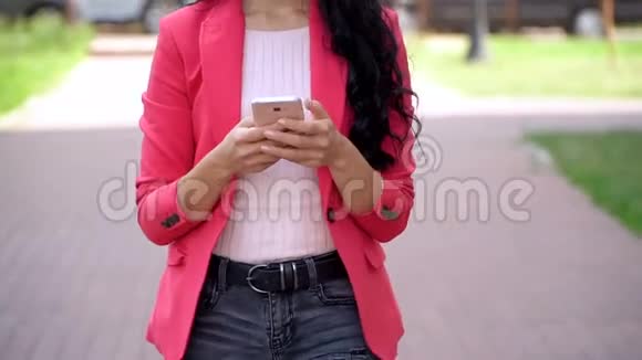 穿红色夹克的苗条女孩在夏天的公园里使用智能手机视频的预览图