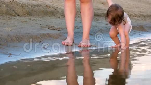 孩子在河边玩耍用手拿湿沙妈妈带着孩子沿着河在海滩上散步视频的预览图