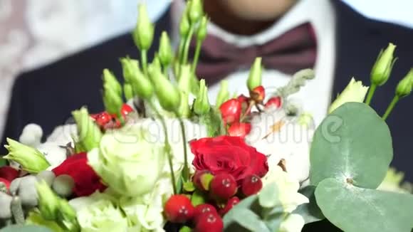 穿着红色领结和白色衬衫的人手里捧着美丽的白玫瑰和红花特写视频的预览图