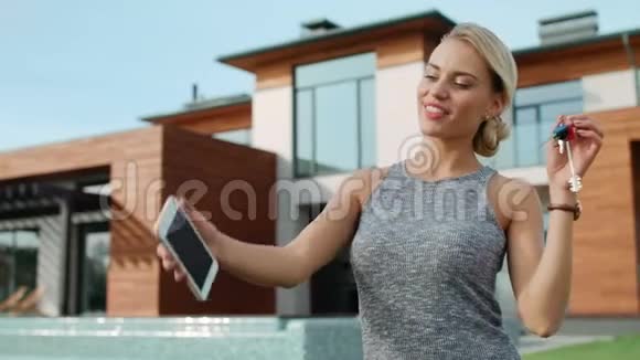 幸福的女人在豪宅附近用房子钥匙自拍视频的预览图