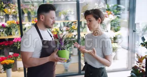 男子持绿色植物与花店女顾客交谈视频的预览图