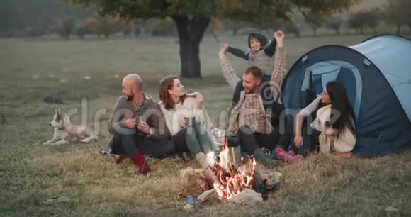 在大自然中两个家庭晚上野餐的时间是篝火在帐篷旁边爸爸在玩他的视频的预览图