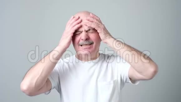 成熟的男人穿着白色t恤闭着眼睛痛苦地摸着他的头视频的预览图