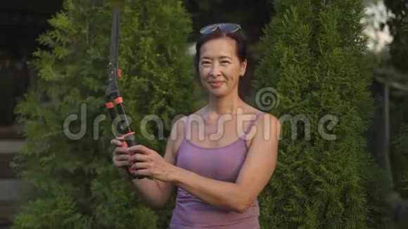 微笑的亚洲女人站在她的花园里与剪刀视频的预览图