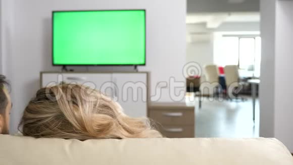 男人和女人舒适地躺在沙发上看着绿色屏幕的电视视频的预览图