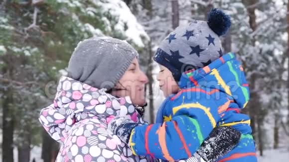 一位快乐的母亲在冬天的一个白雪覆盖的森林或公园的背景下拥抱和亲吻她的孩子情绪视频的预览图