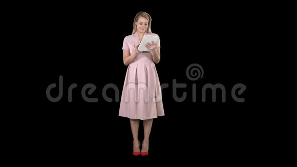 穿着粉色连衣裙拿着平板电脑看着它的漂亮年轻女子阿尔法频道视频的预览图