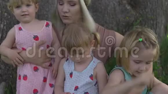 年轻的金发嬉皮妈妈和她的小女孩在公园的树下坐着笑视频的预览图