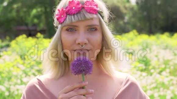 一位年轻的金发嬉皮女子的肖像戴着鼻环头发上戴着洋红色的花带手里拿着洋葱紫花视频的预览图