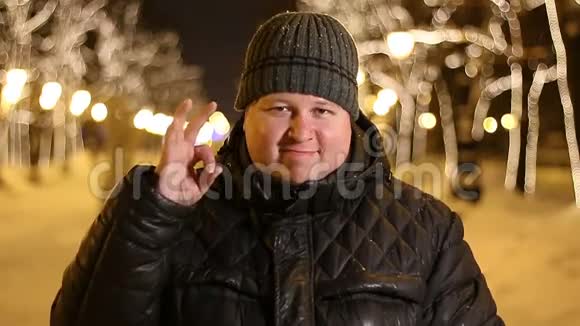 冬天寒冷的夜晚快乐的男人在户外展示OK标志的肖像视频的预览图