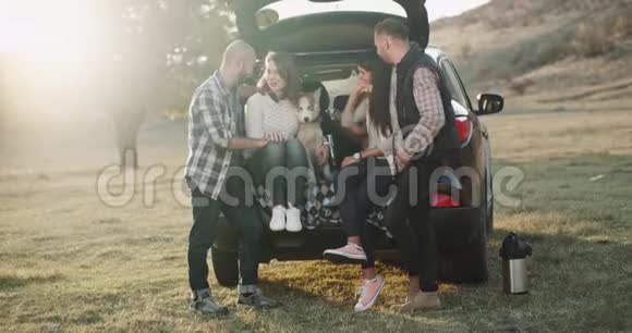 在汽车的后备箱里两对夫妇和一只哈士奇狗在大自然的中间度过了美好的时光4k视频的预览图