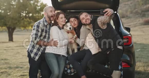 有魅力的夫妻在一次汽车旅行中有一个停留用手机拍摄一些自拍照片他们坐在汽车的后备箱里视频的预览图