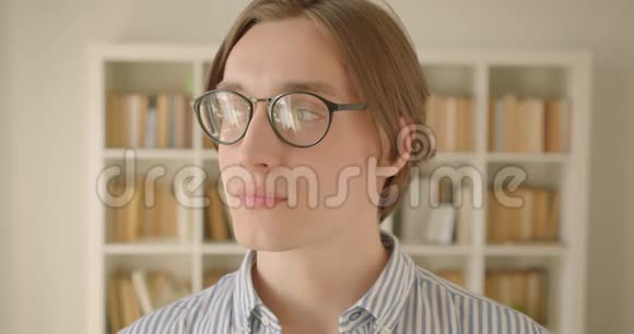 年轻漂亮的白种人男学生戴着眼镜看着镜头欢快地笑着的特写照片视频的预览图