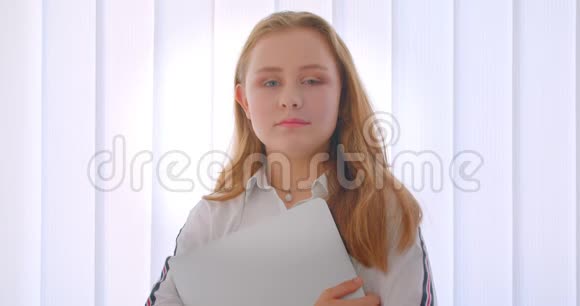 一位年轻漂亮的白种人女孩手里拿着一台笔记本电脑站在公寓里的特写肖像视频的预览图