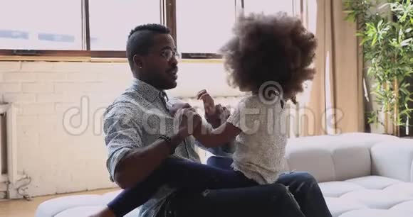 非洲爸爸笑着和沙发上可爱的女儿玩视频的预览图