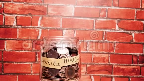 满是硬币钱的玻璃罐在砖的背景上旋转以揭示紧急情况房子储蓄和退休的话视频的预览图