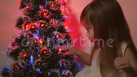 女儿在圣诞树上检查花环小孩子在儿童房的圣诞树旁玩耍美丽的人造的视频的预览图