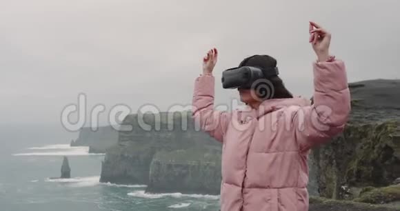 在悬崖顶上戴着虚拟现实眼镜的女人VR女士玩得很开心周围风景优美视频的预览图