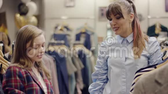 年轻有魅力的女人向漂亮的女售货员展示她的智能手机屏幕以找到她想买的裙子视频的预览图