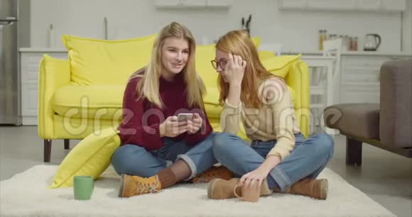 快乐的女性朋友在家分享智能手机视频的预览图