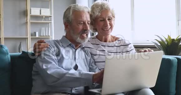 老人家庭祖父母夫妇用手提电脑聊天坐在沙发上视频的预览图
