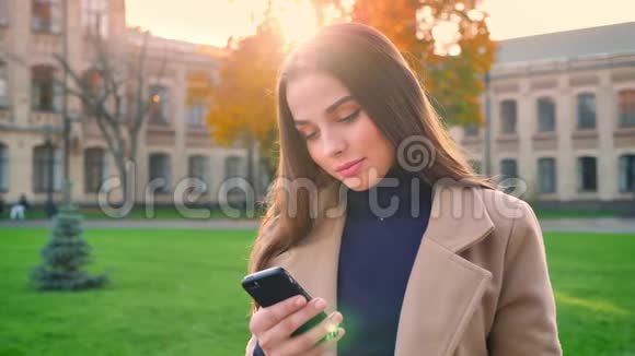 在白天和阳光明媚的时候一位充满自信的白种人女性正集中精力在她的手机里站立和打字视频的预览图