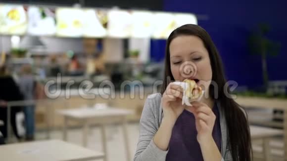 饥饿的女人在购物中心的食物场吃饭一位年轻的美女在快餐店嚼着美味的热狗视频的预览图