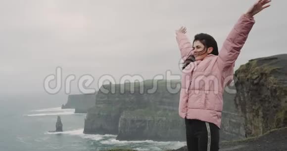 悬崖顶上漂亮的年轻女士很高兴欣赏海洋和风景她非常高兴和视频的预览图