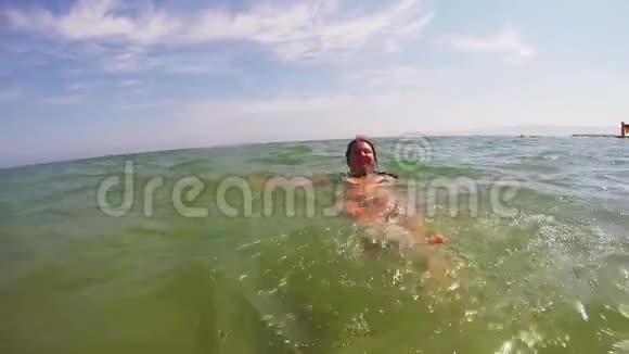 一个穿着黑色泳衣的快乐女人在海边的海面上漂浮视频的预览图