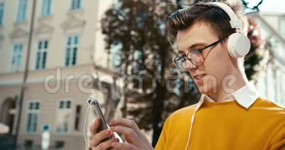 戴着耳机和眼镜的青少年坐着通过手机聊天和浏览的画像视频的预览图