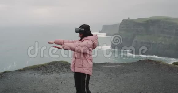 在悬崖的屋顶上年轻的女士戴着虚拟现实眼镜开心地玩着她用虚拟现实做了一个游戏视频的预览图