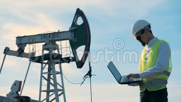 一个有笔记本电脑的人在靠近油泵的油田工作视频的预览图